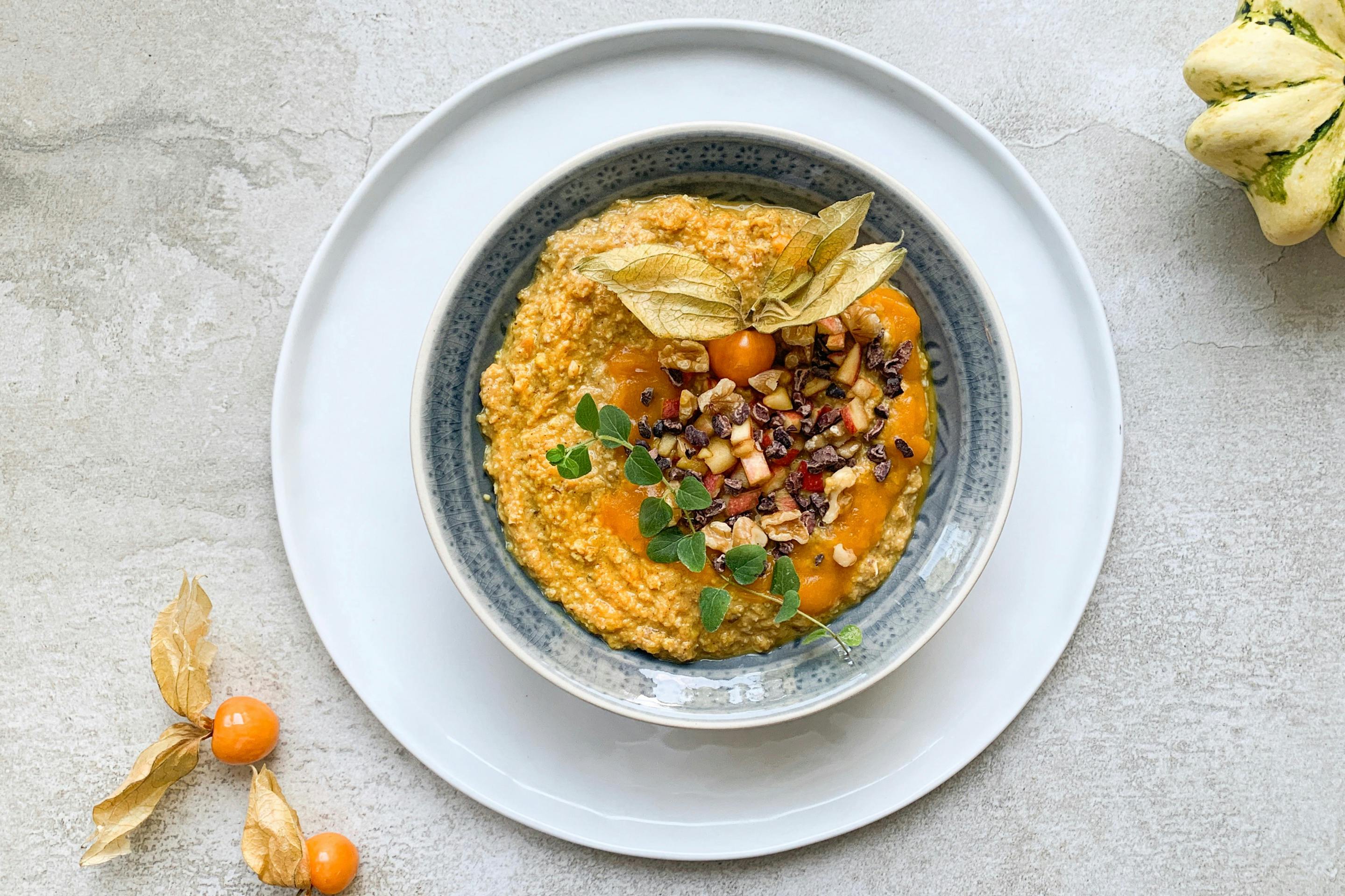 Goldenes Kürbis Porridge auf einem Teller angerichtet mit Physalis verziert