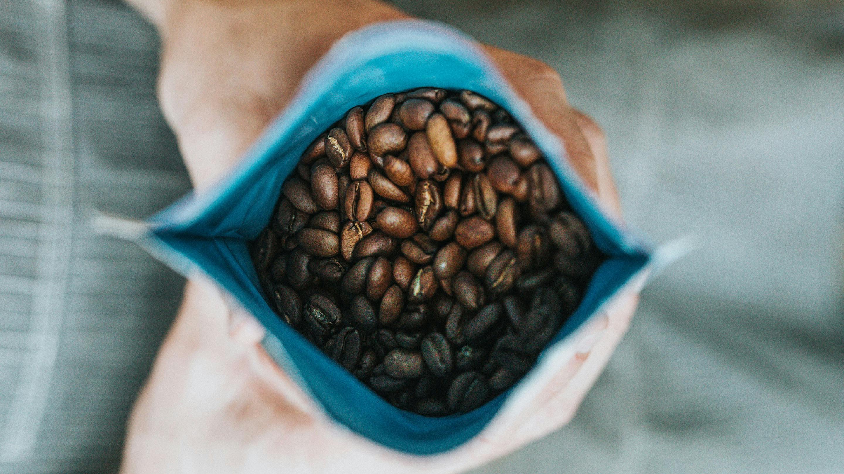 2 Hände halten einen Beutel mit frischen Kaffeebohnen