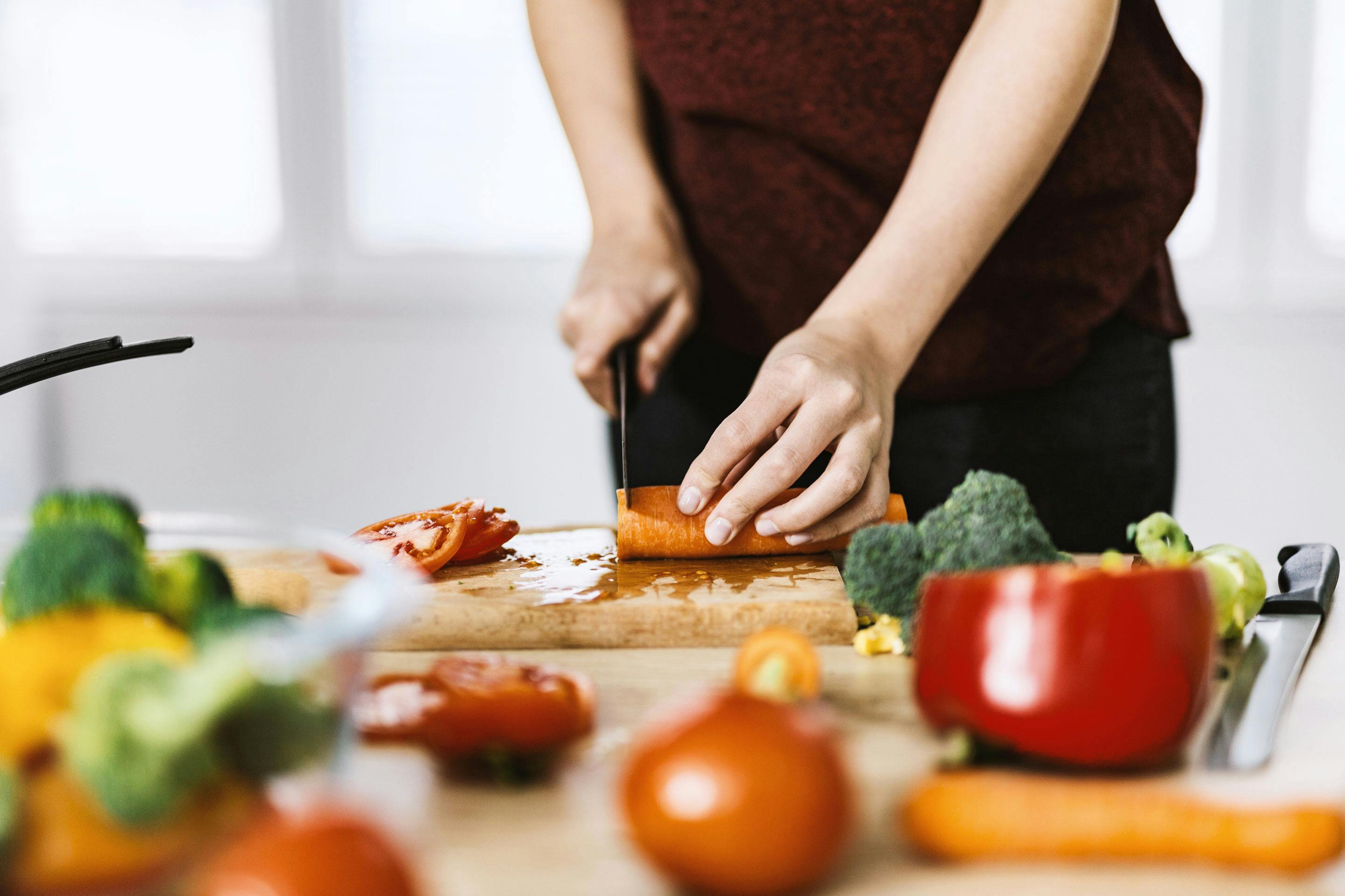 eine Frau mit dunkelroter Schürze schneidet Karotten, Tomaten und anderes Gemüse auf einem Brett