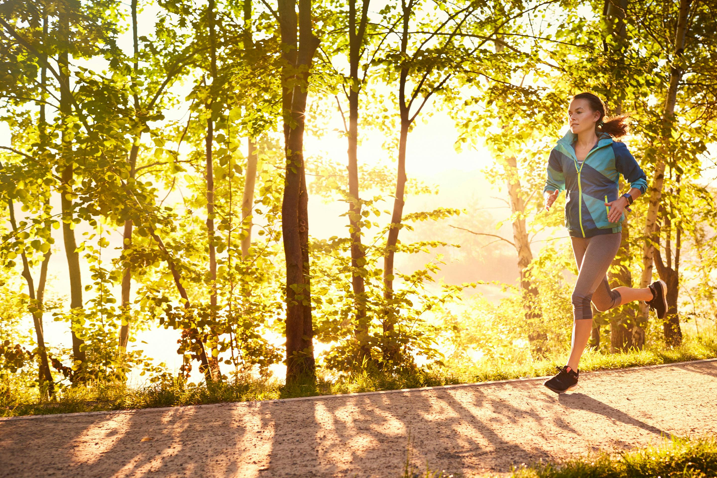 eine Frau beim Joggen durch einen Licht durchfluteten Laubwald