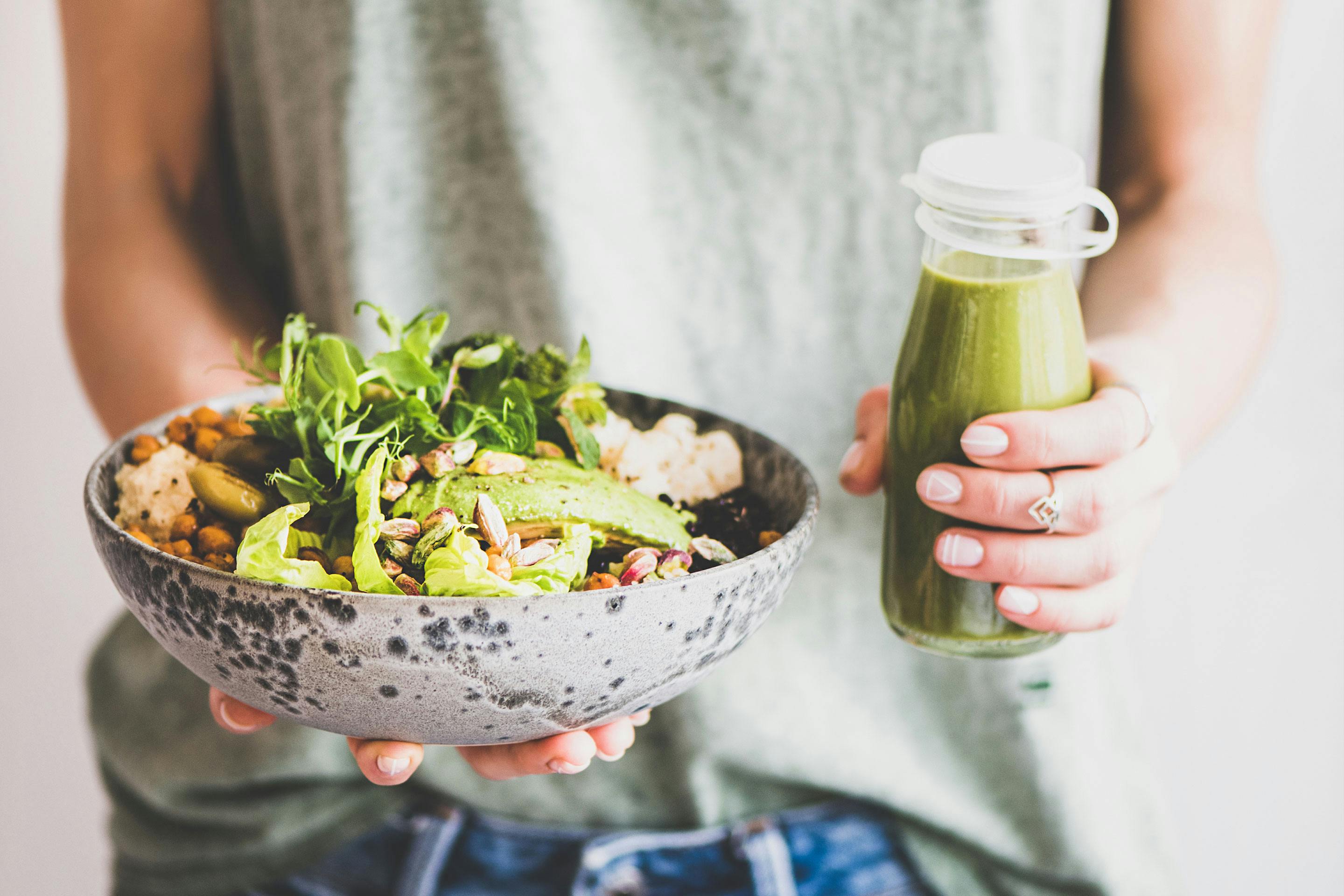 Eine Frau hält eine Bowl mit Gemüse und Reis und einen grünen Smoothie in beiden Händen