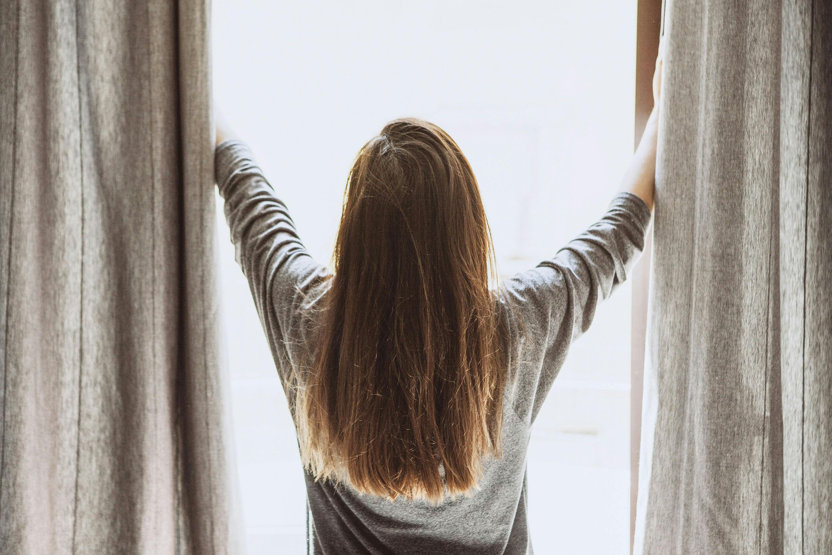 Eine Frau zeiht die Vorhänge vor einem Fenster auf