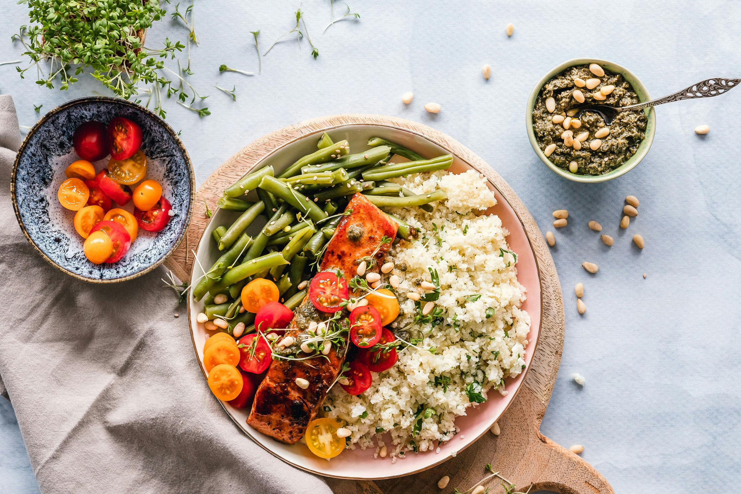 Ein Teller mit Fisolen, Cocktailtomaten und Quinoa auf einem runden Holzbrett