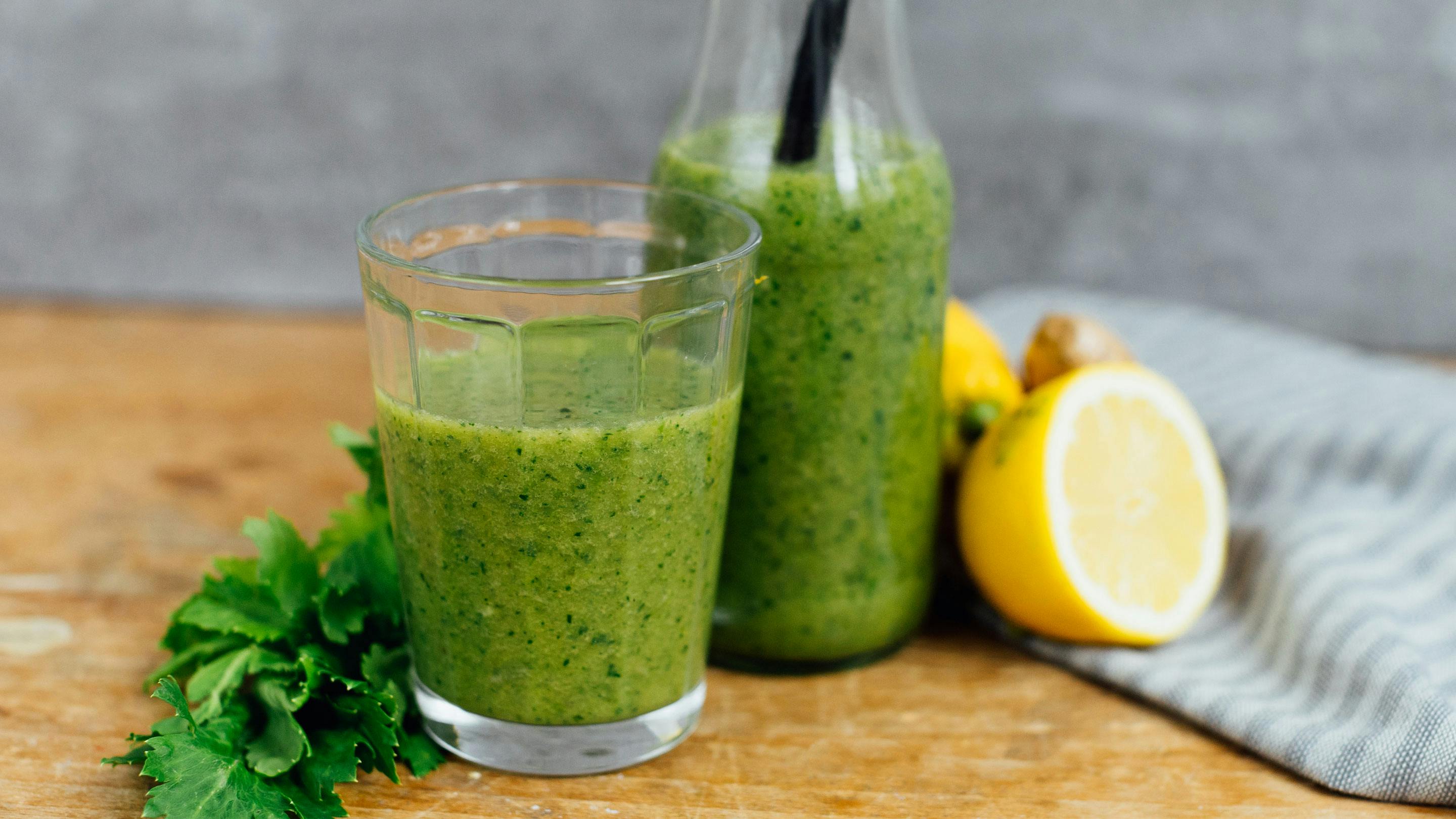 grüner Smoothie im Glas und Fläschchen auf einem Holzbrett