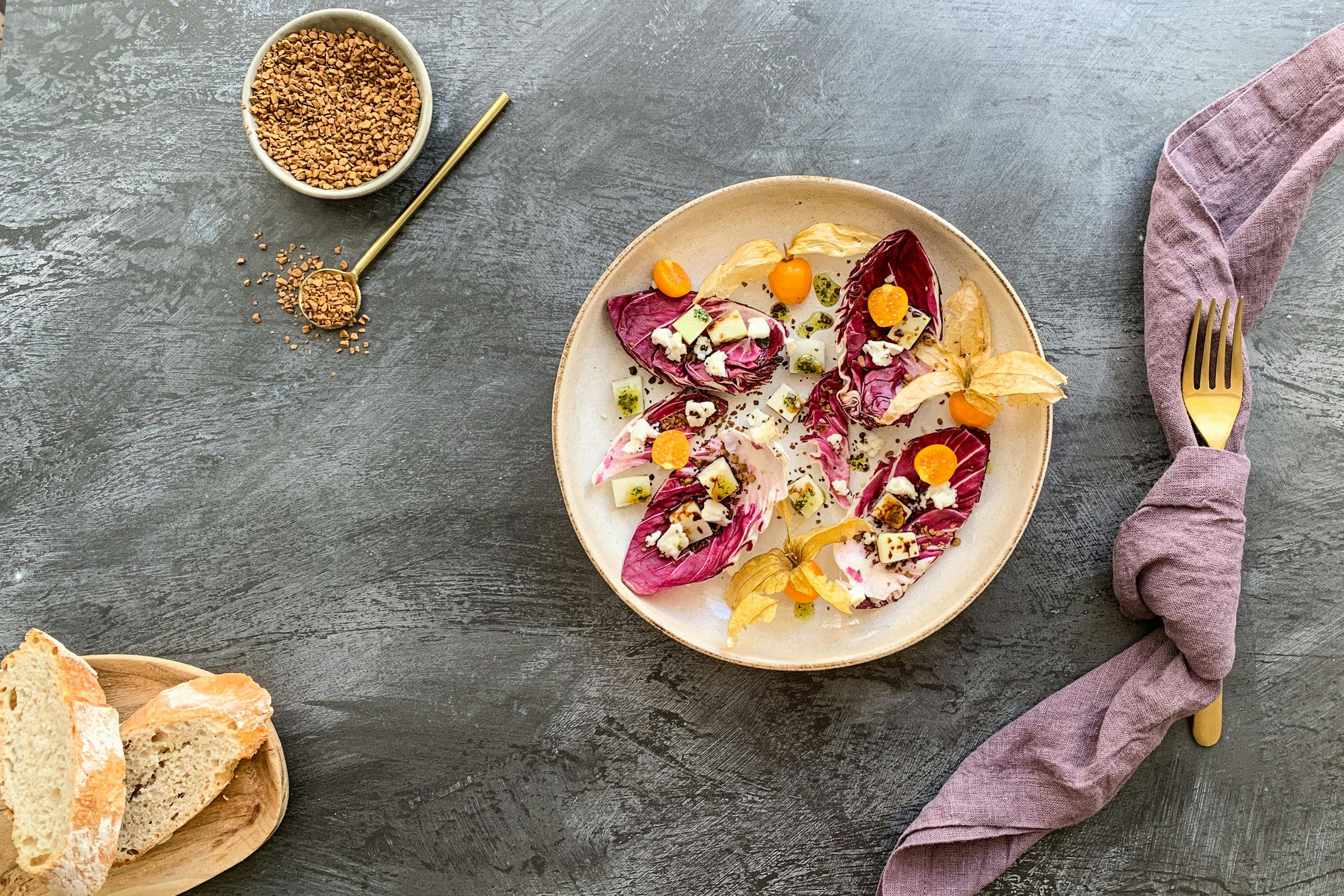 Radicchio Salat mit Kohlrabischeiben und Physalis auf einem beigen Teller mit Brot und Serviette angerichtet