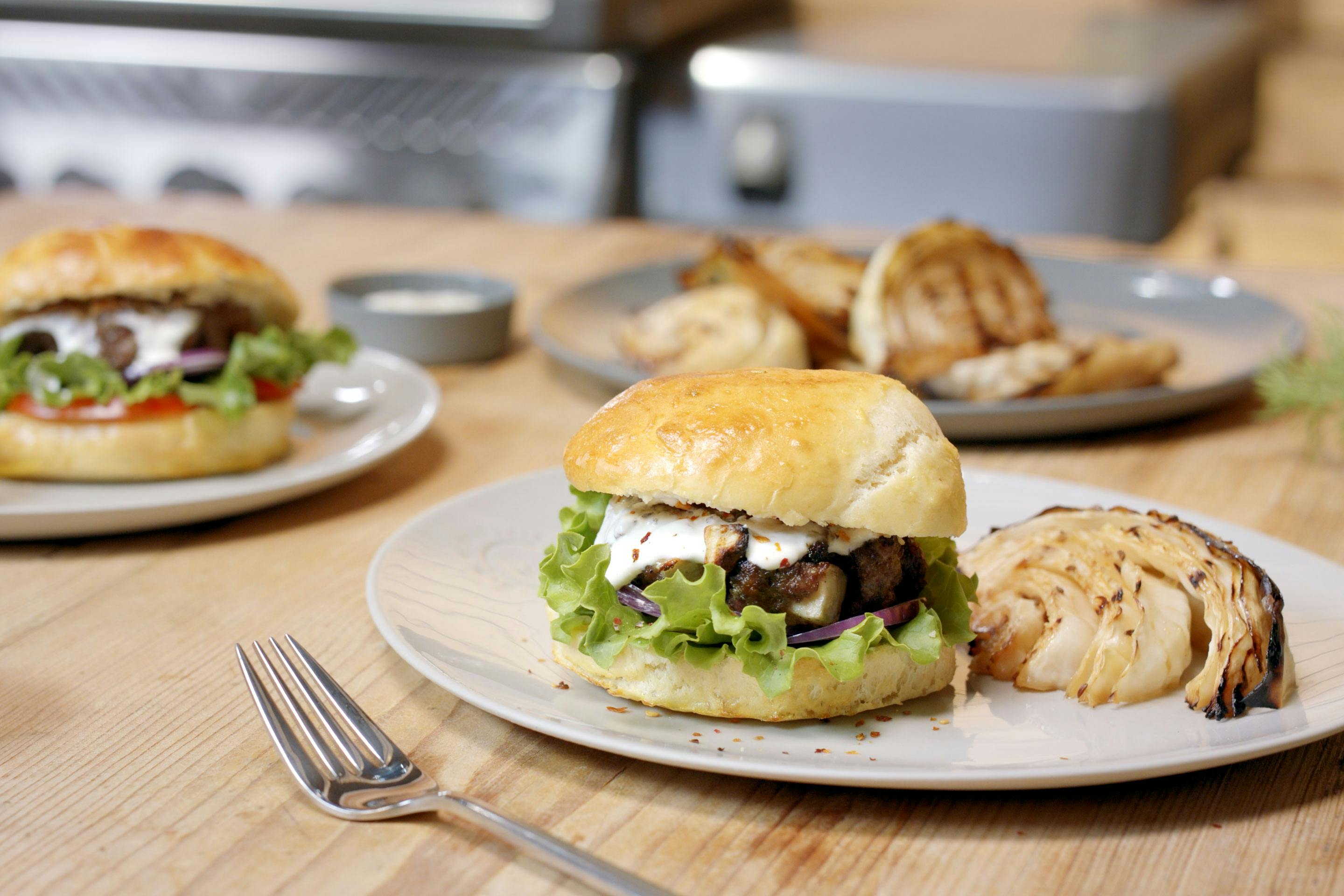 Burger mitKäse-Röstzwiebel-Patty und gegrilltem Krautkopf auf einem hellen Teller auf einem Holztisch