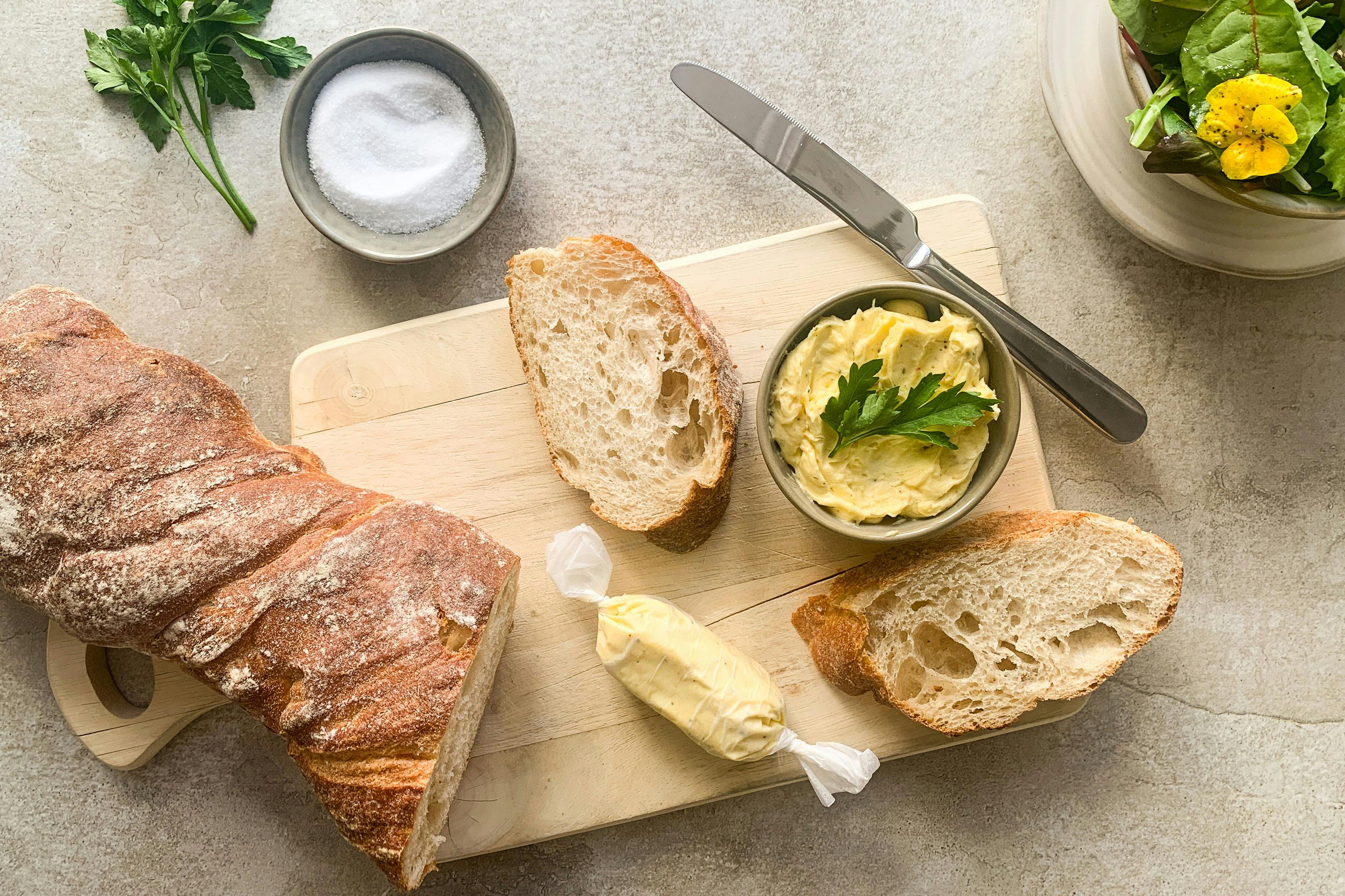 Honig-Senf-Butter mit Soja Sauce auf einem Holzbrett mit Buttermesser, Baguette und frischem grünen Salat