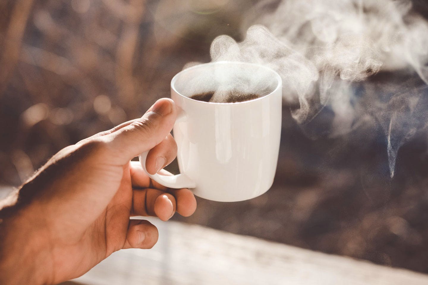 eine Hand hält eine Tasse mit dampfendem Kaffee
